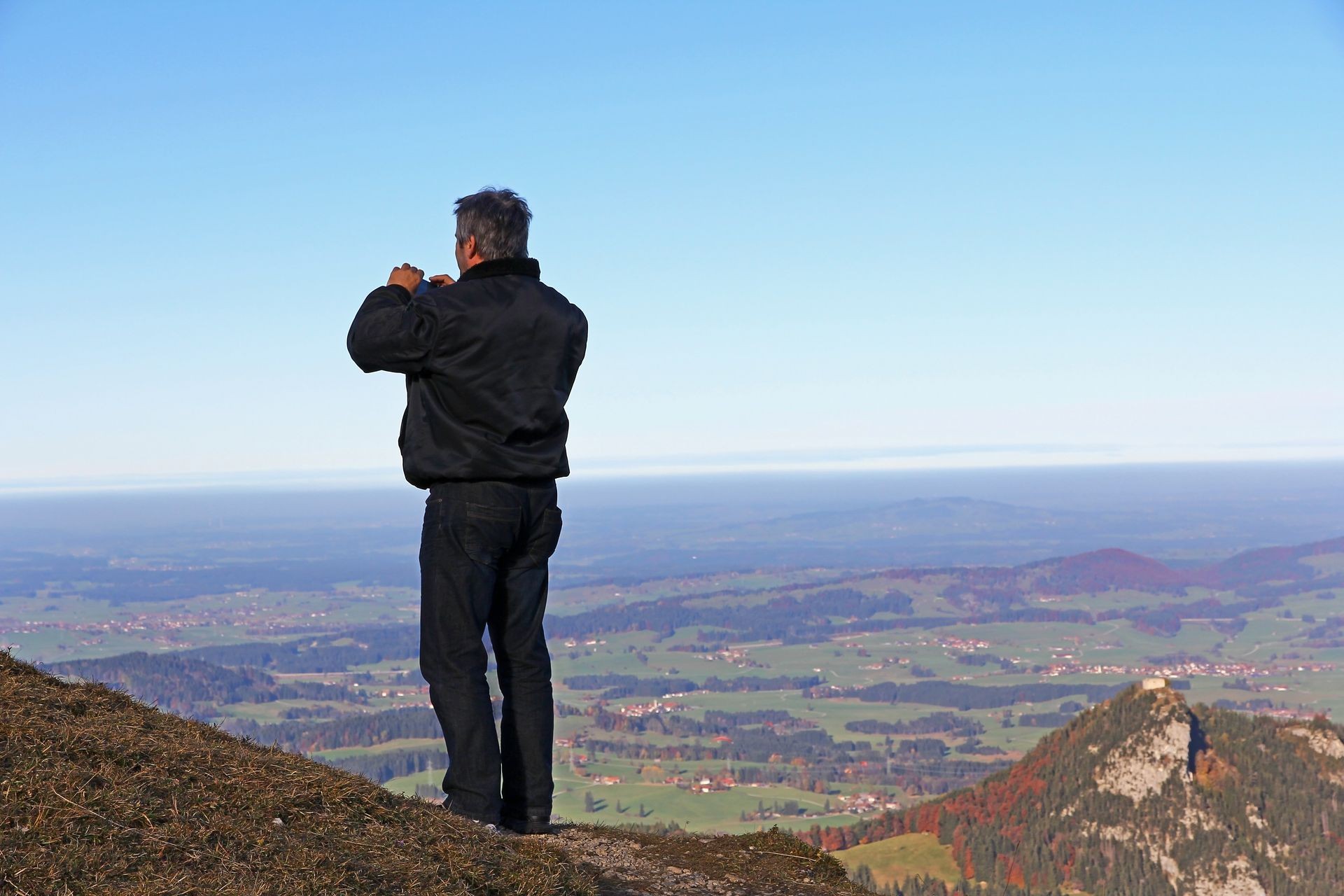 A man takes a picture of the view down a mountain with his mobile phone
